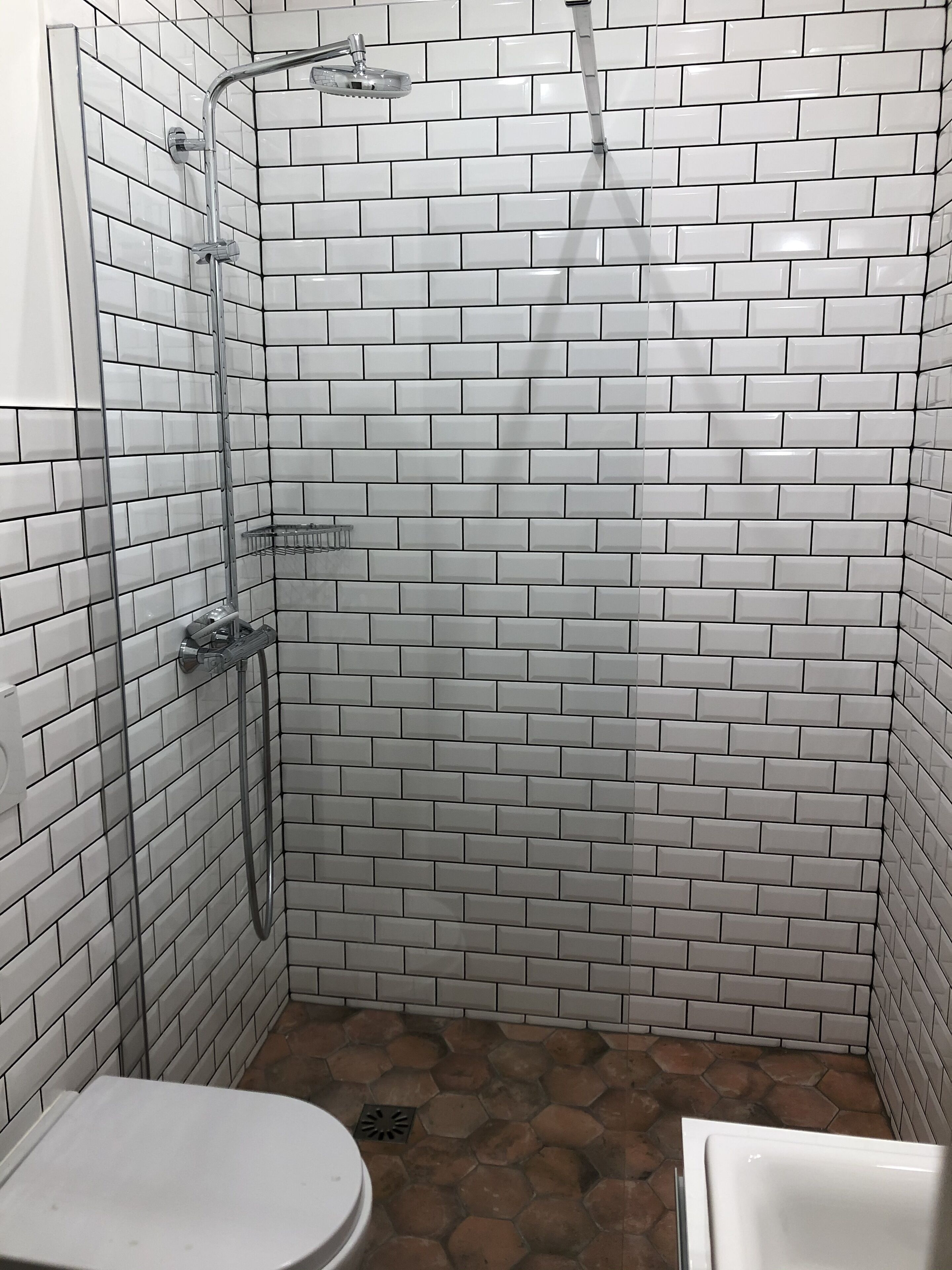 A bathroom with white subway tiles, a shower with a handheld showerhead, and a toilet.