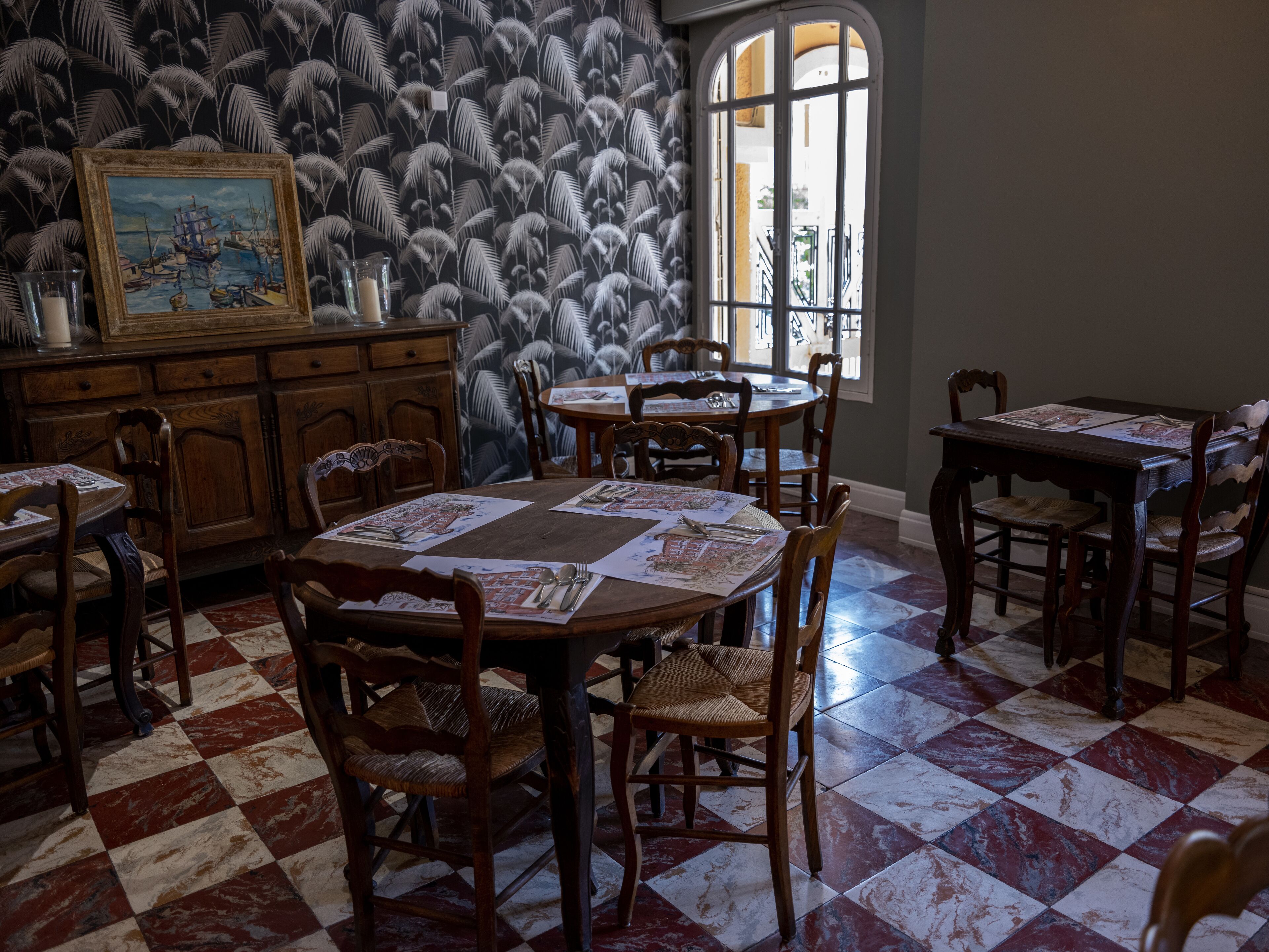Un espace repas avec des tables et des chaises en bois, un papier peint à motifs et un tableau accroché au mur.