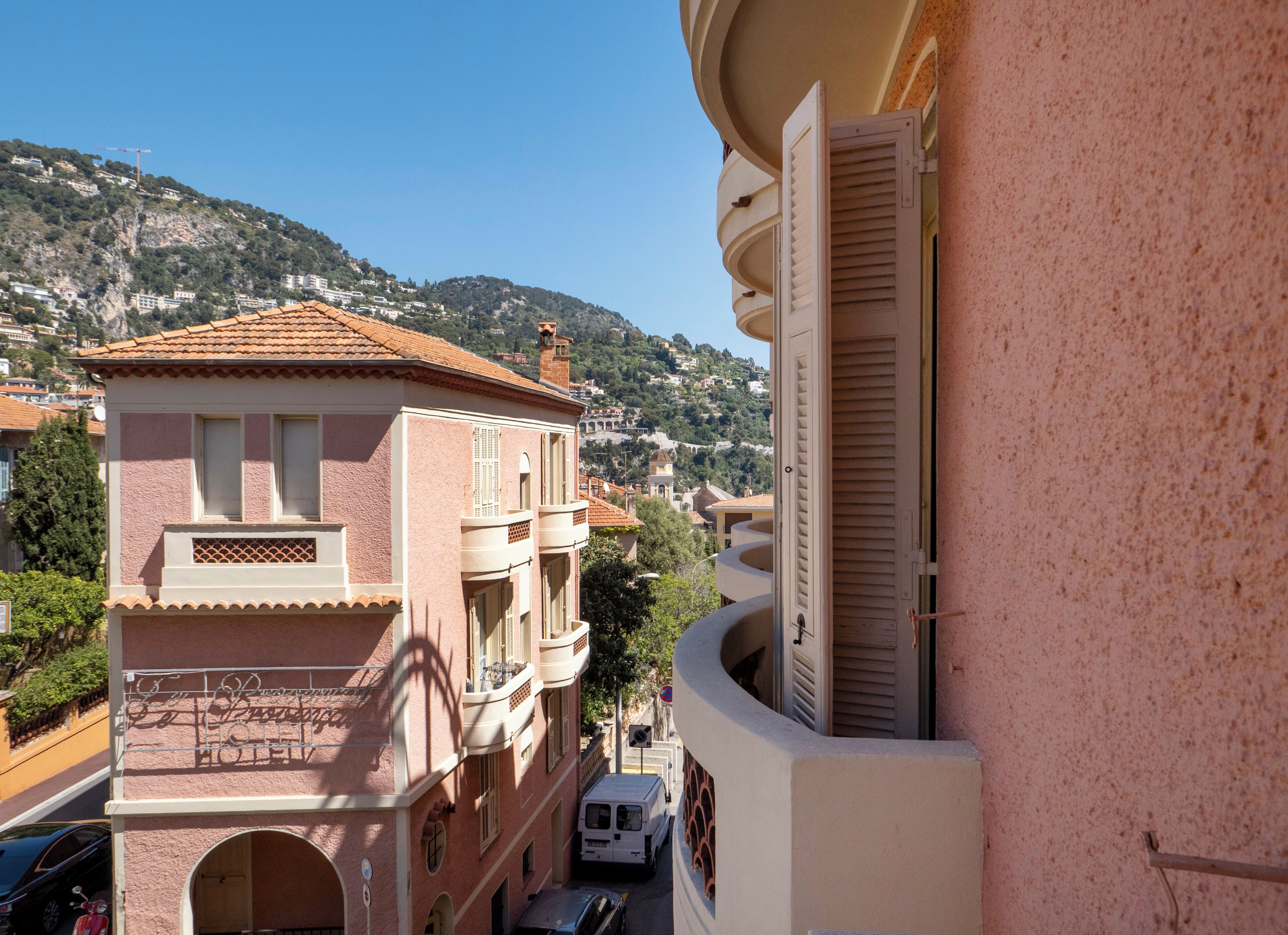 A multi-story building with balconies, a clear sky, and a mountainous backdrop.