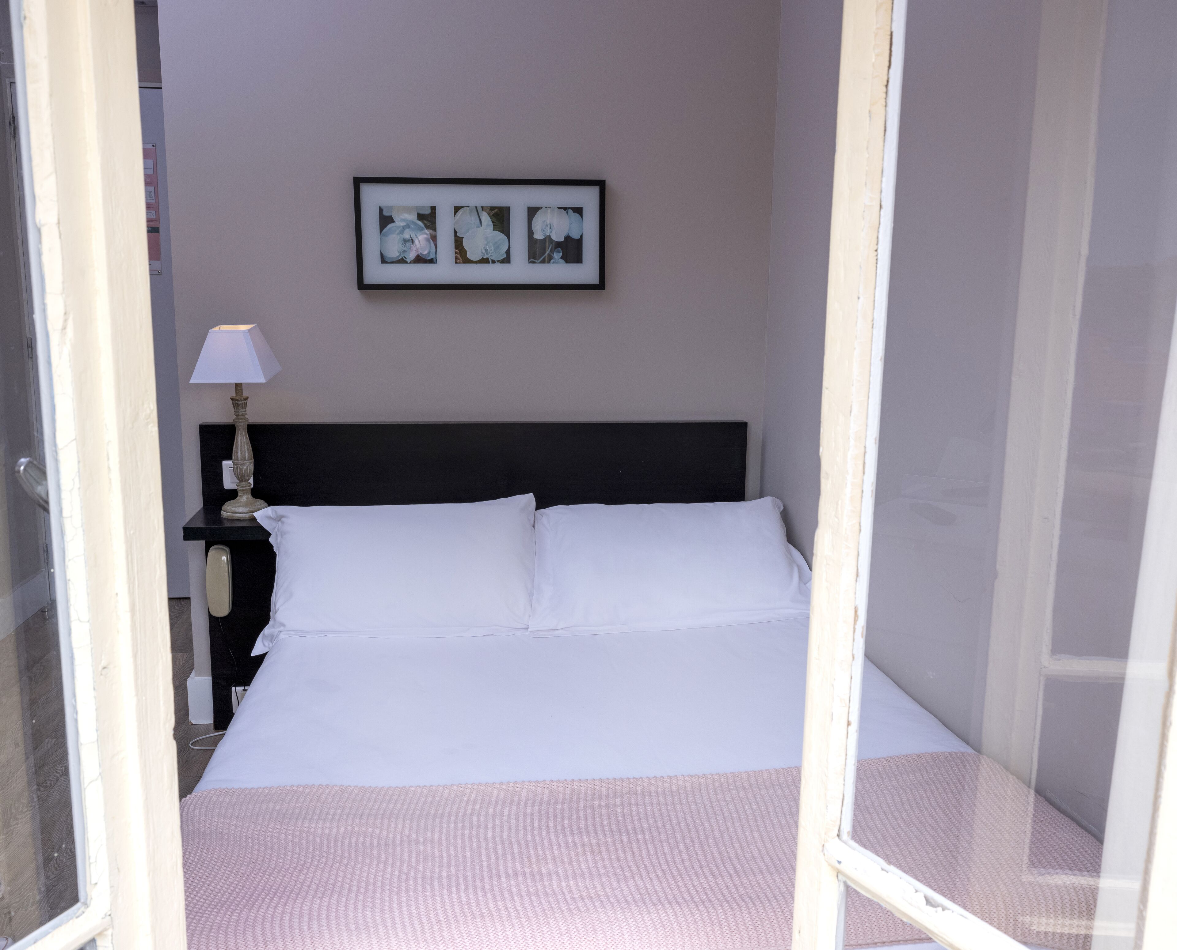 A neatly made bed with white linens, a bedside table with a lamp, and a framed picture on the wall.