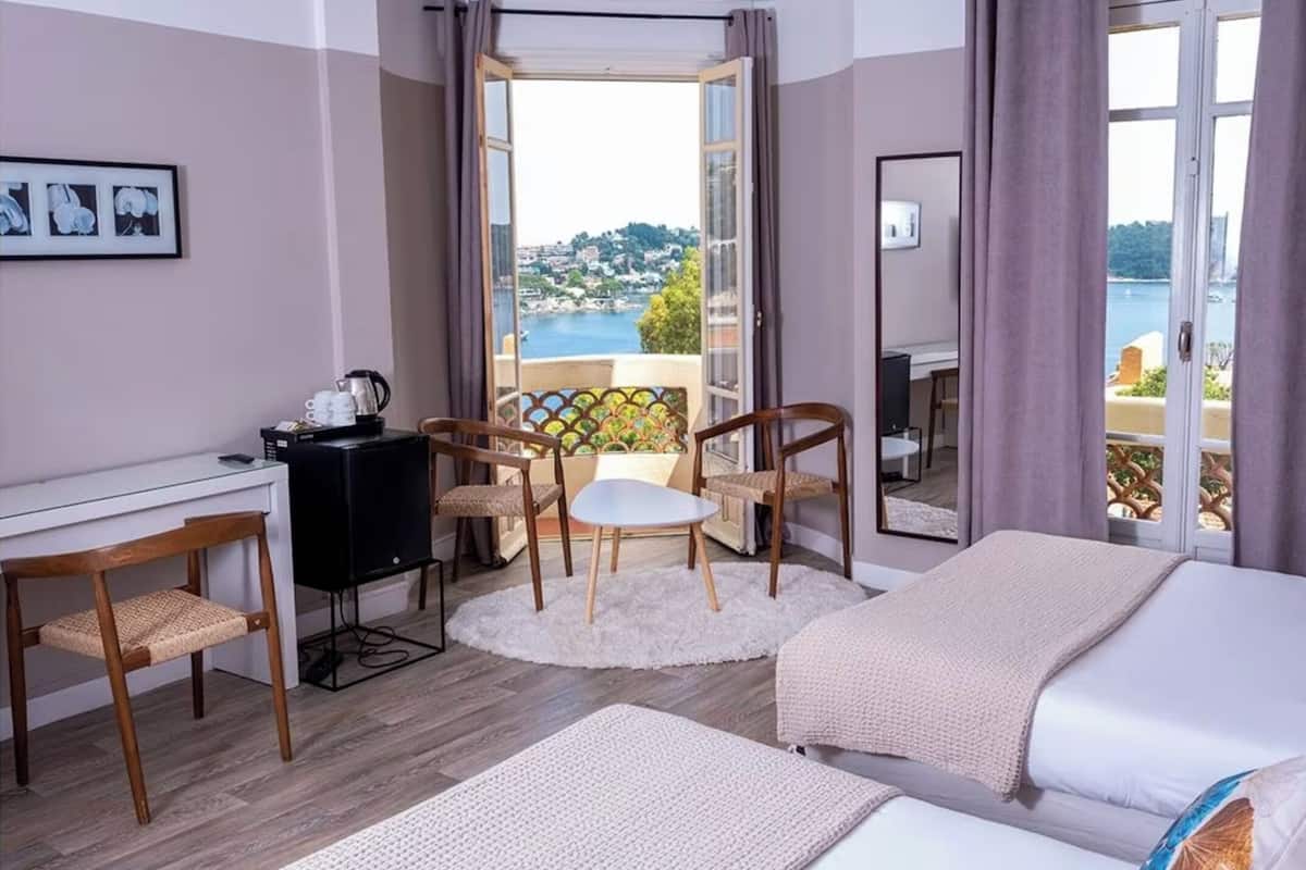 A hotel room with a bed, a desk, a chair, and a view of the sea.