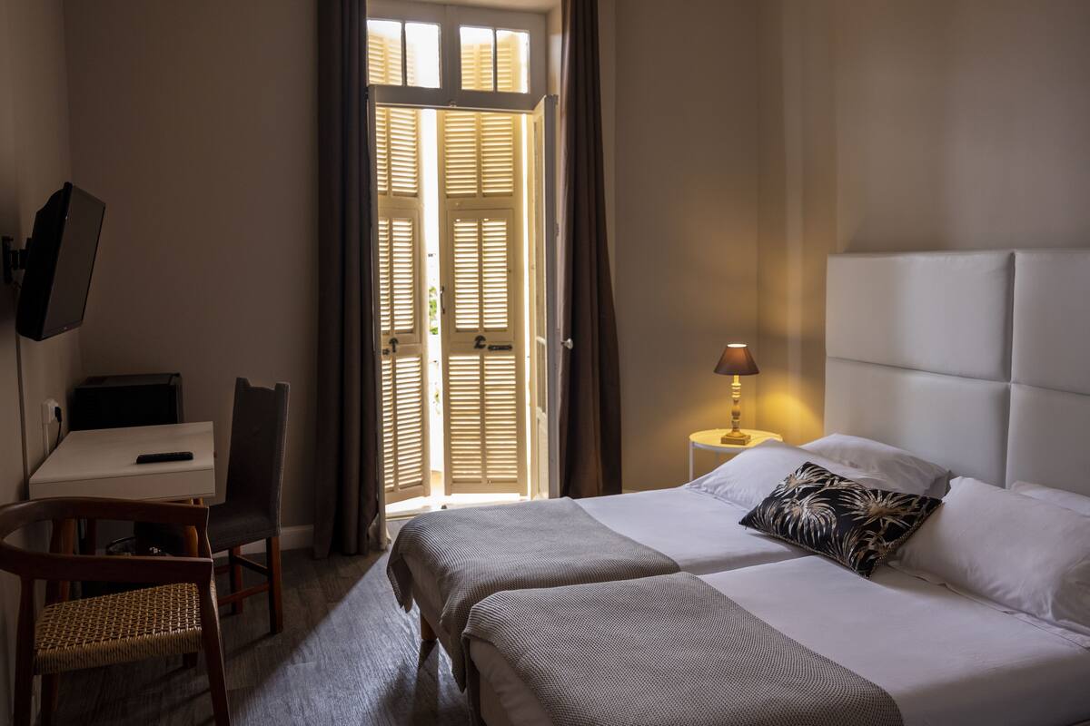 A hotel room with two beds, a desk, a chair, a TV, and a lamp.