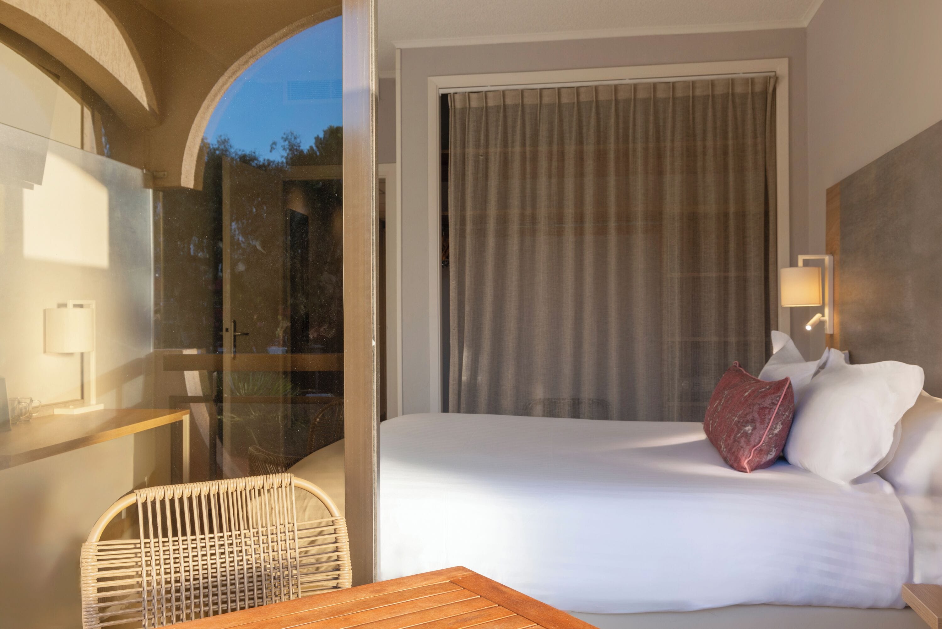 A hotel room with a bed, a chair, a table, and a large window with curtains.