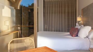 A hotel room with a bed, a chair, a table, and a large window with curtains.