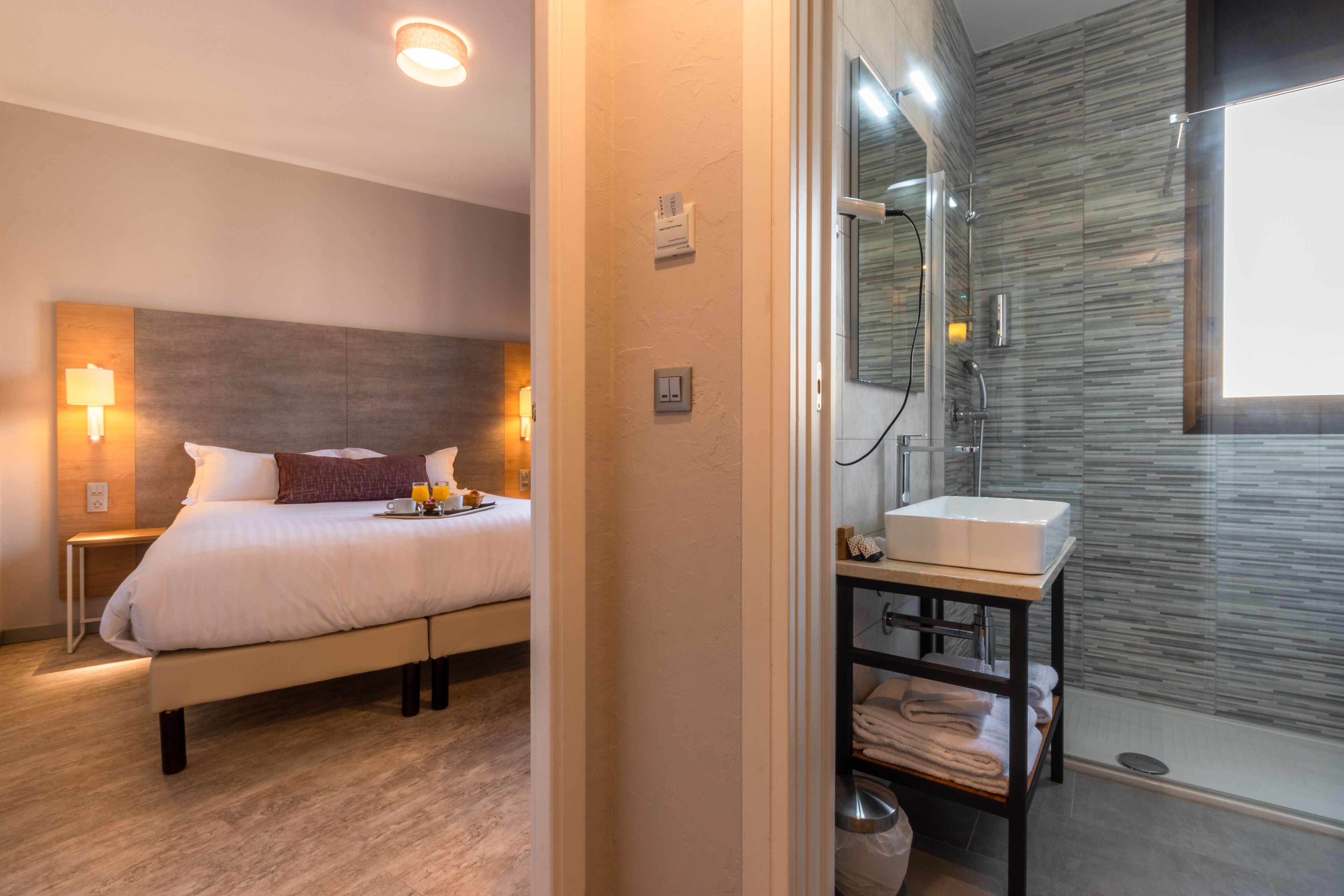 A modern hotel room with a large bed, bedside lamps, a bathroom with a glass shower, and a sink.