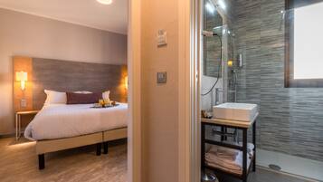 A modern hotel room with a large bed, bedside lamps, a bathroom with a glass shower, and a sink.