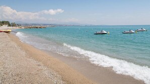 Una playa con agua turquesa cristalina, orilla pedregosa y varios jet skis a lo lejos.