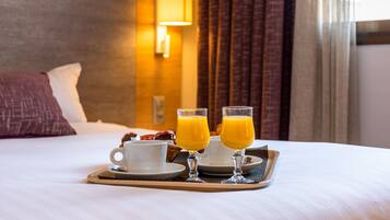Una cama bien hecha con una bandeja de desayuno que incluye dos vasos de jugo de naranja y una taza de café.