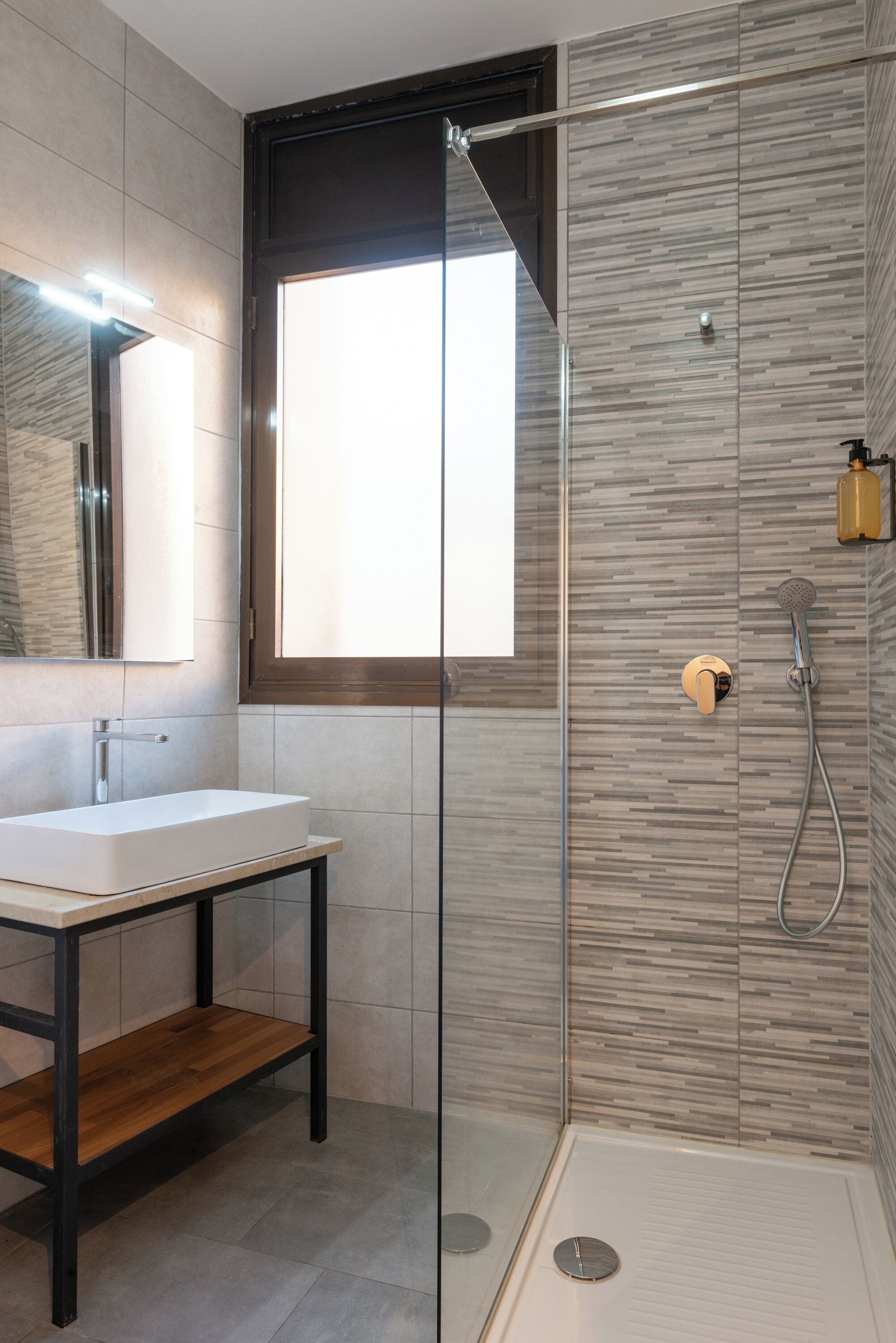 Un bagno moderno con cabina doccia in vetro, uno specchio grande e un mobile bagno in legno.
