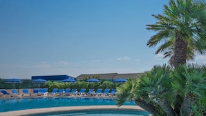 Una piscina con sillas reclinables azules y sombrillas, rodeada de palmeras.
