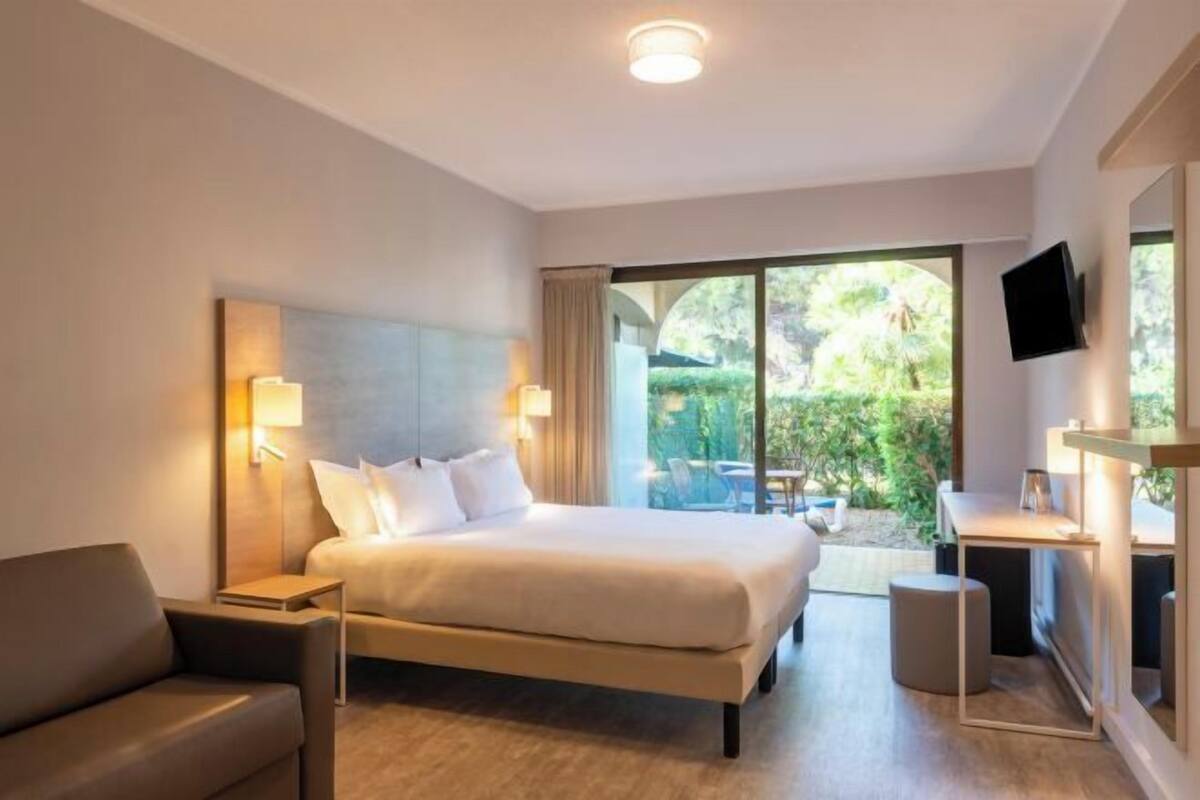 A modern hotel room with a large bed, a sofa, a desk, and a TV.