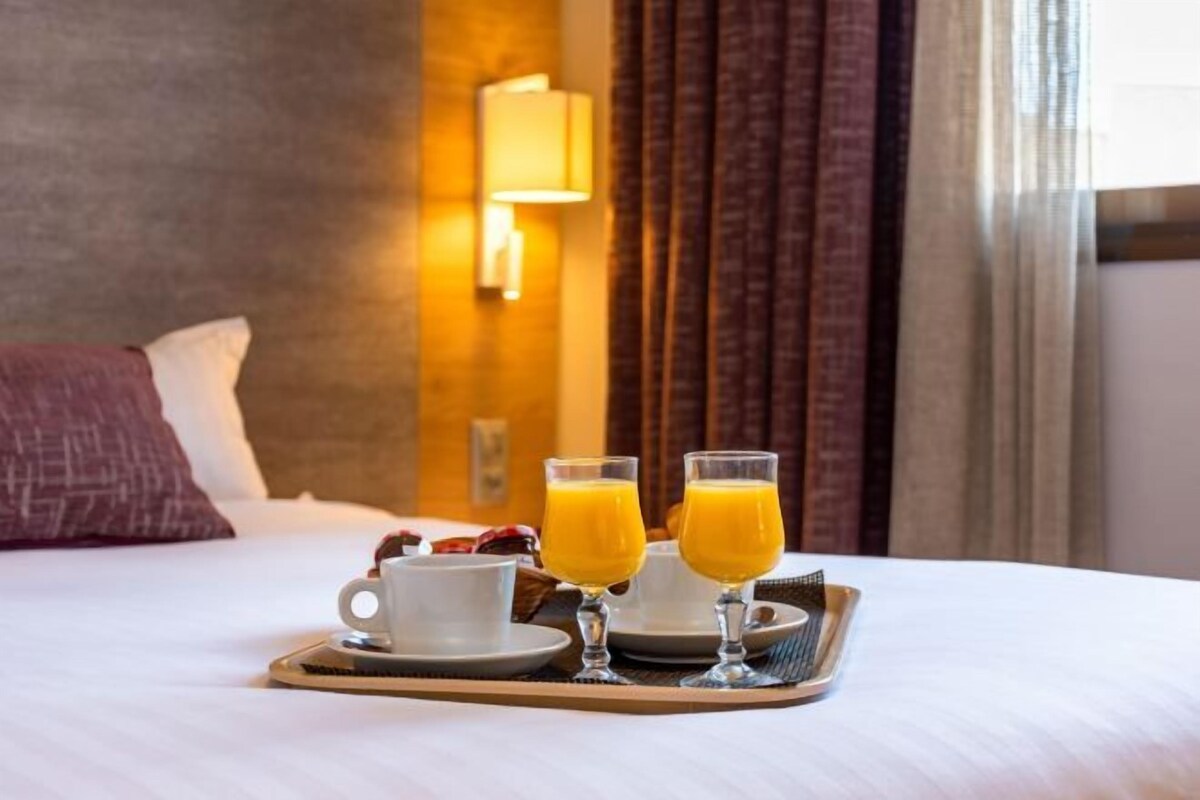 A hotel room with a bed, a tray with two glasses of orange juice, a cup, and a plate.