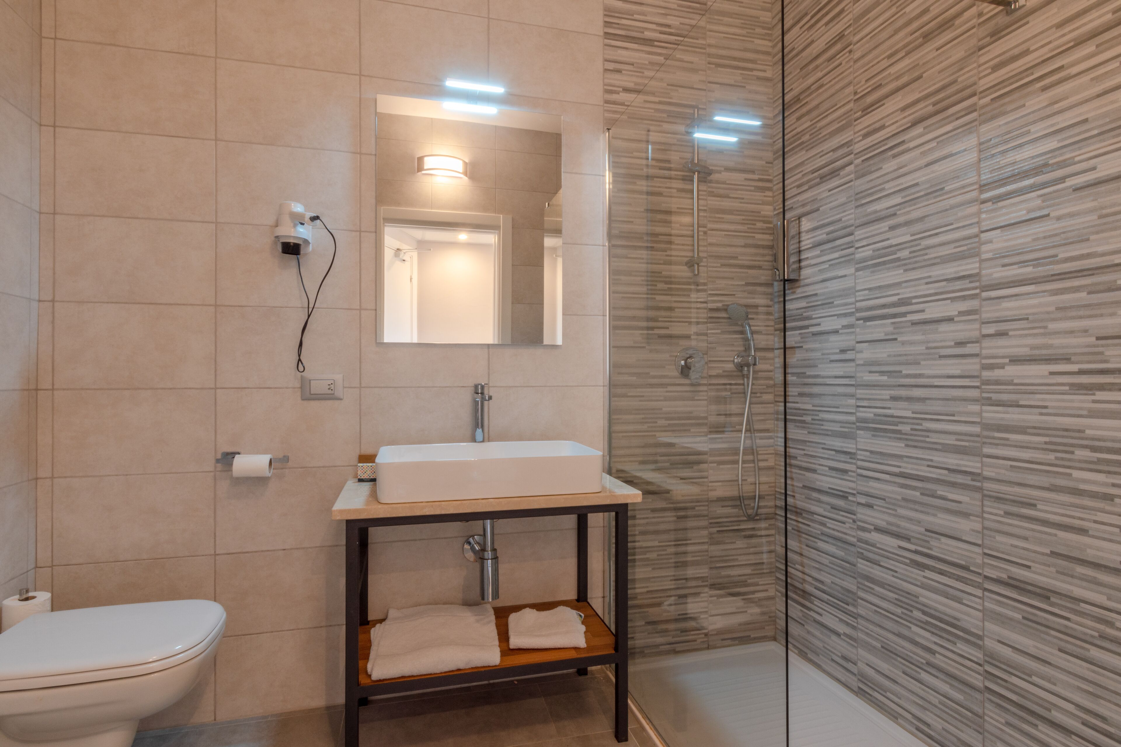 A modern bathroom with a toilet, sink, mirror, and glass shower enclosure.