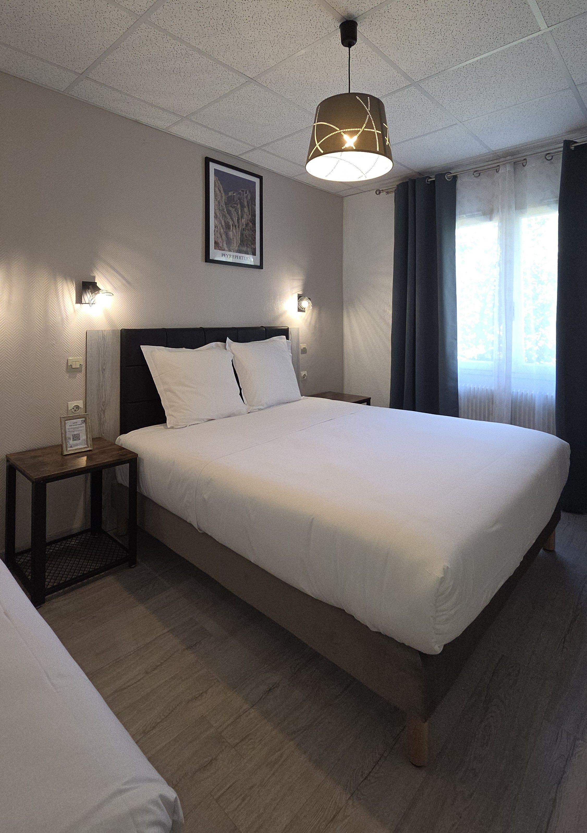 Ein Hotelzimmer mit einem großen Bett, einem Nachttisch, einer Wandleuchte und einem gerahmten Bild.
