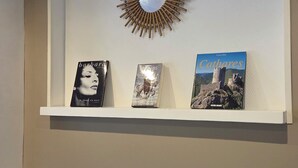 A living room with a fireplace, a wall-mounted shelf with books, and a decorative sunburst mirror. - HOTEL RESTAURANT MAS LE CHATELET (Saint-Paul-de-Fenouillet)
