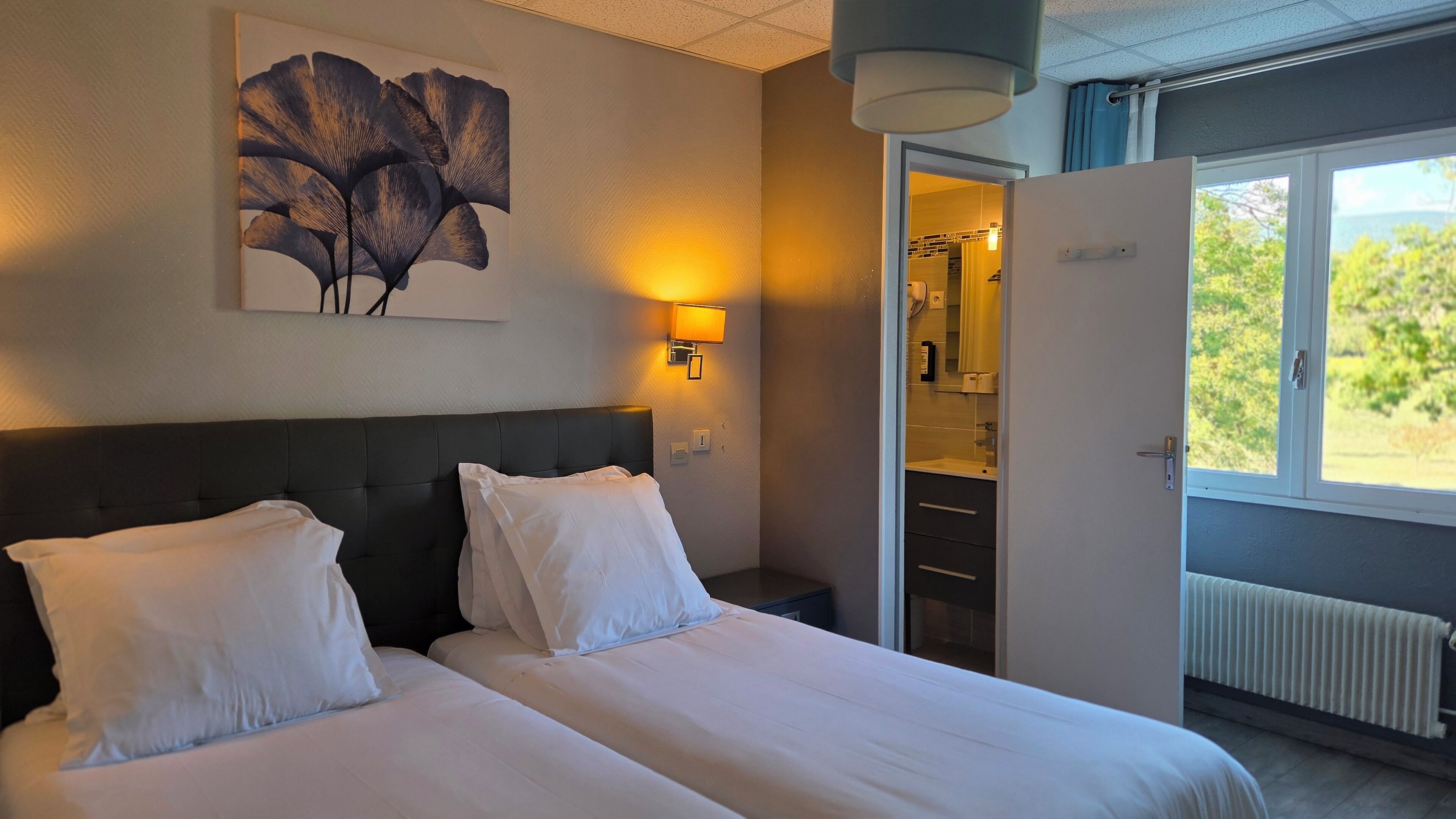 Hotelkamer met een groot bed, nachtkastje, wandlamp en uitzicht op de omgeving.