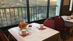 Una mesa dispuesta con cruasanes, tazas de café y cubiertos, con vistas a un paisaje pintoresco.