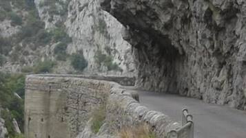 Una carretera de montaña estrecha y serpenteante, bordeada por muros de piedra y terreno rocoso.