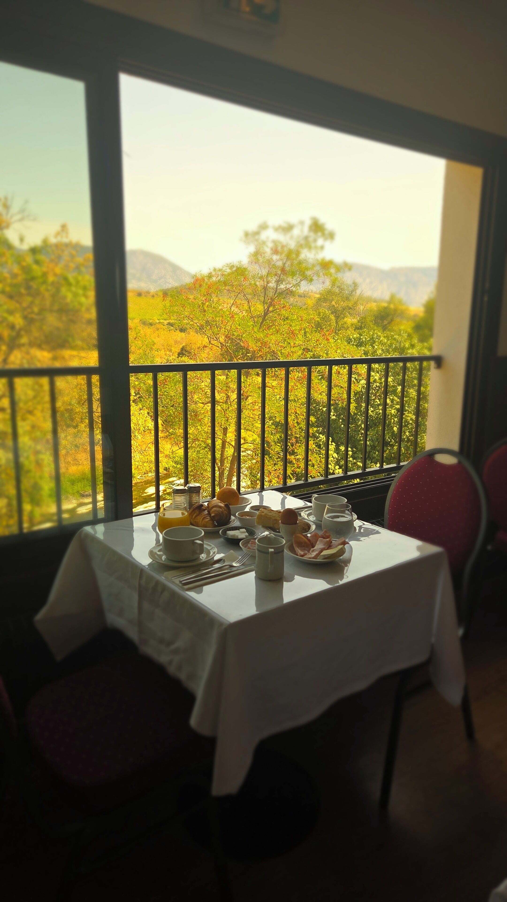 A dining table set with breakfast items, a view of a mountainous landscape through a balcony railing.