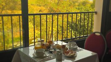 A dining table set with breakfast items, a view of a mountainous landscape through a balcony railing.