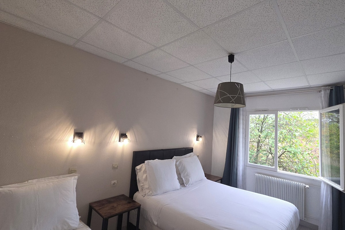 Una habitación de hotel con cama, mesita de noche, lámpara, ventana y televisión en la pared.