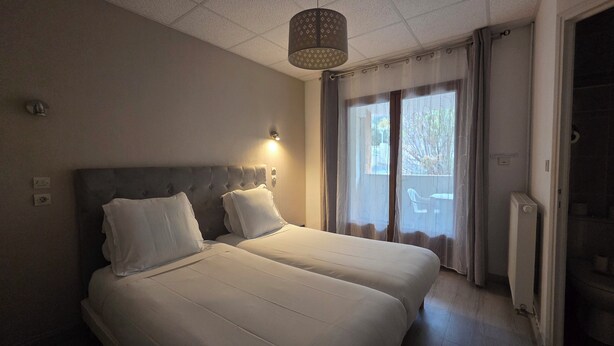 Habitación de hotel con dos camas, una lámpara en el techo, una ventana con cortinas y un radiador.