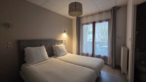 Une chambre d’hôtel avec deux lits, un luminaire au plafond, une fenêtre avec des rideaux et un radiateur.