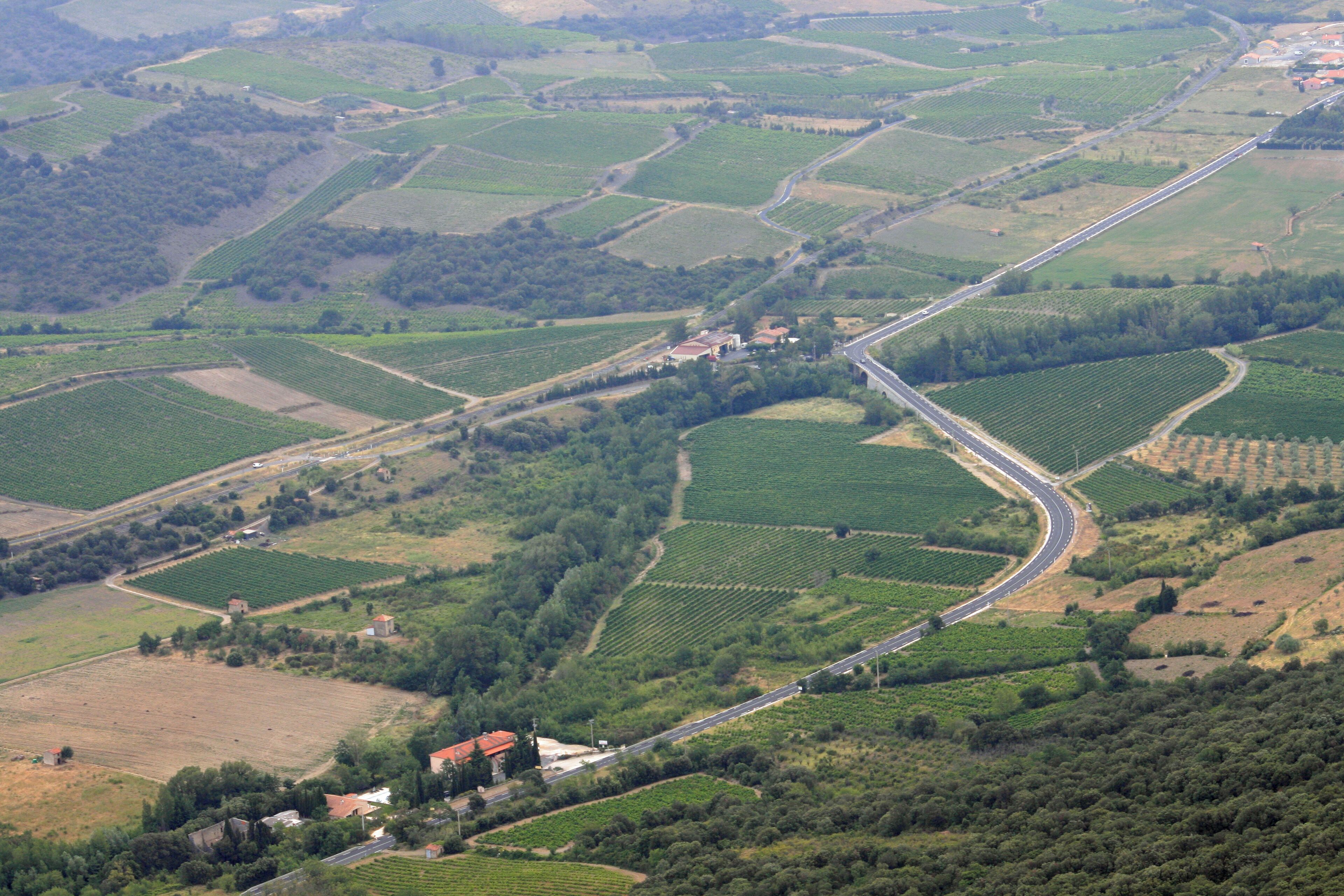 A rural landscape with terraced fields, a winding road, and a small settlement with buildings.