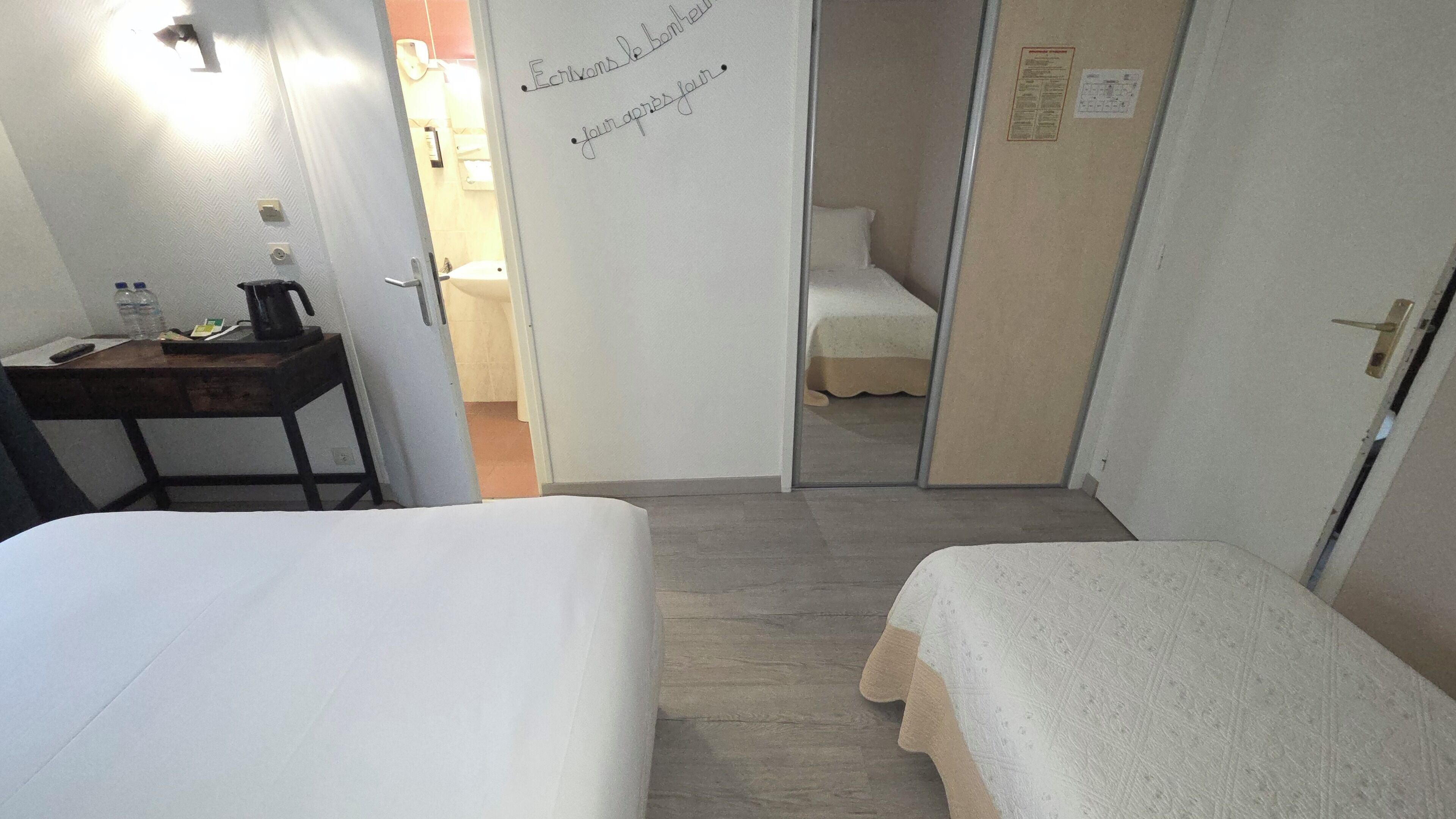 A hotel room with a bed, a desk with a lamp, and a door leading to a bathroom.