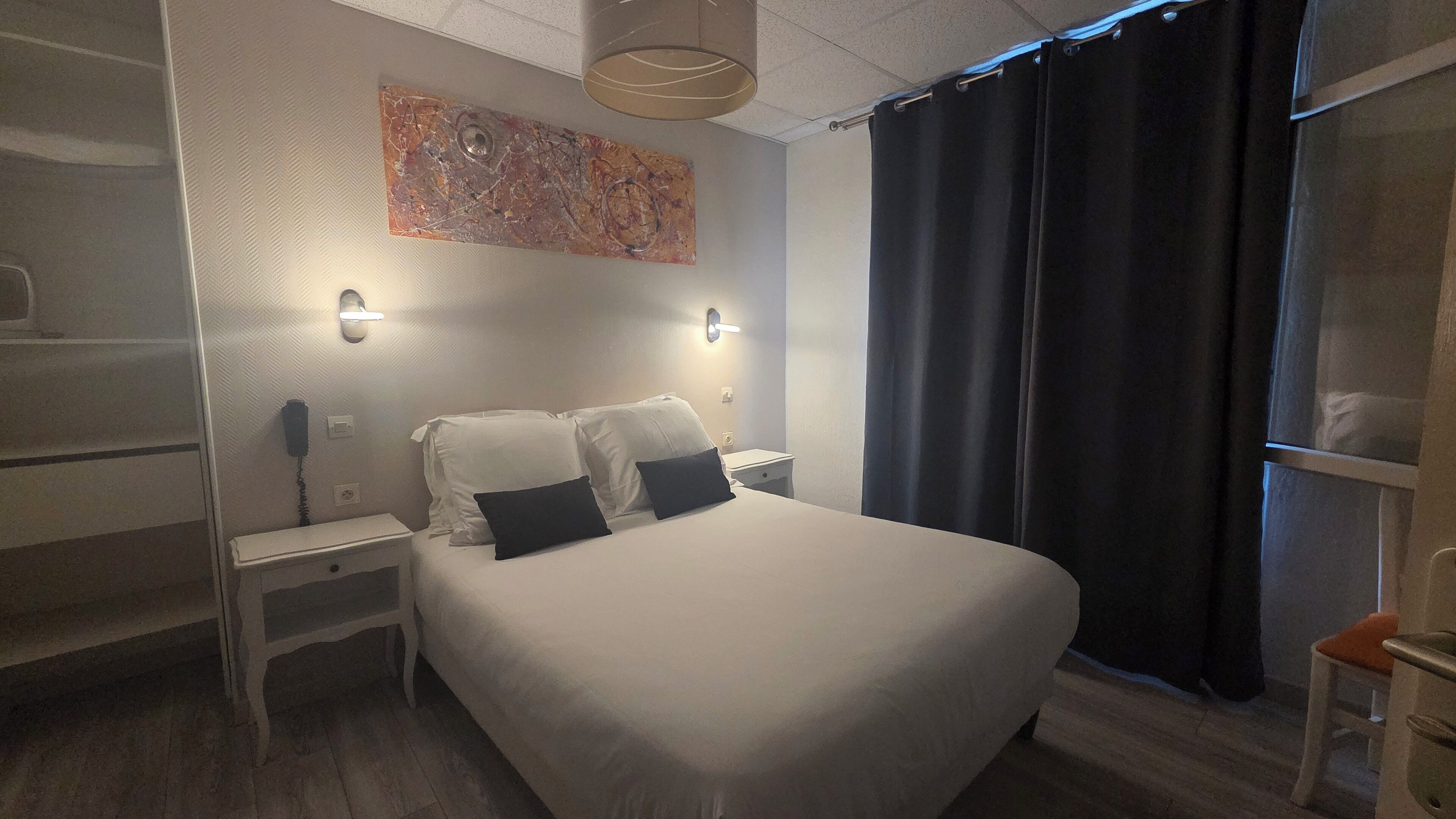 Una camera d'albergo con un letto grande, due comodini, un'opera d'arte appesa al muro e una finestra con tende scure.