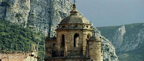 Un edificio de piedra con una cúpula y ventanas de arco, rodeado de acantilados rocosos y vegetación.