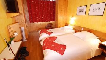 Een hotelkamer met twee bedden, een televisie, een rood gordijn en een houten vloer.