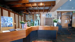 A reception area with a wooden counter, a digital sign, and a wall-mounted menu board. - Hôtel Carlit (Font-Romeu-Odeillo-Via)