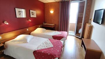 Habitación de hotel con dos camas, cabecera de madera, televisor montado en la pared y puerta corrediza de vidrio al exterior.