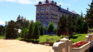 A large, multi-story hotel with a classic architectural style, surrounded by a well-maintained garden and trees.
