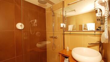 A modern bathroom with a glass shower enclosure, a white sink, and a glass-topped vanity.