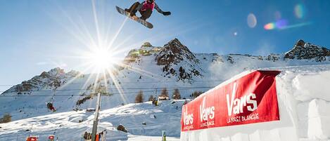 A snowboarder performing a jump over a snow ramp with a red advertisement for 'VARS' in the background.