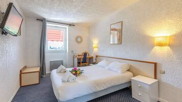 Habitación de hotel con cama, mesitas de noche, escritorio con silla, televisor y ventana con cortinas.