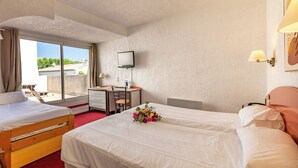 Ein Hotelzimmer mit zwei Betten, einem Schreibtisch, einem Stuhl, einem Fernseher und einem Fenster mit Blick auf Gebäude und Grünflächen.