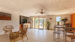 Eine geräumige Lobby mit einer Rezeption, Korbsesseln, einem Essbereich mit Metalltischen und einem Deckenventilator.