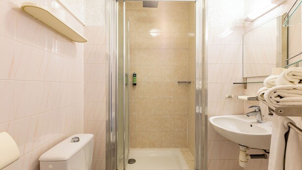 A bathroom with a glass-enclosed shower, a toilet, a sink, and a towel rack. - Logis Héraclée (Saint-Gilles)
