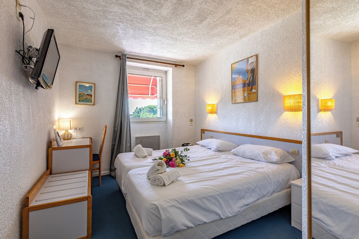 Hotellihuone, jossa on suuri sänky, työpöytä tuolilla, peili ja ikkuna, jossa on verhot.