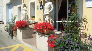 Ein Hotel namens „HOTEL HERACLEE“ mit Außenbereich, einer Frauenstatue und roten und violetten Blumen.