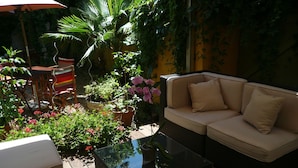 An outdoor seating area with a wicker sofa, a glass coffee table, and various potted plants. - Hôtel des Arceaux (Montpellier)