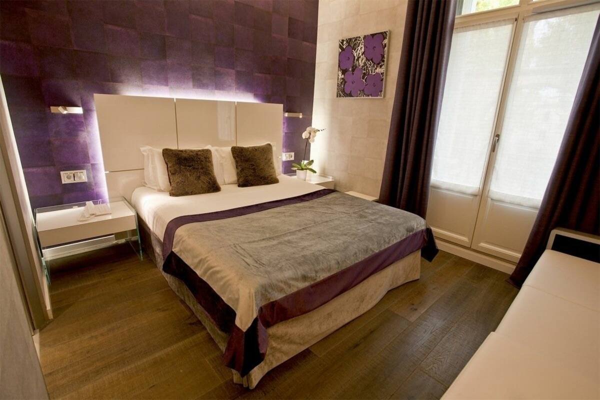 A modern bedroom with a large bed, a nightstand, a bedside table, and a window with curtains.