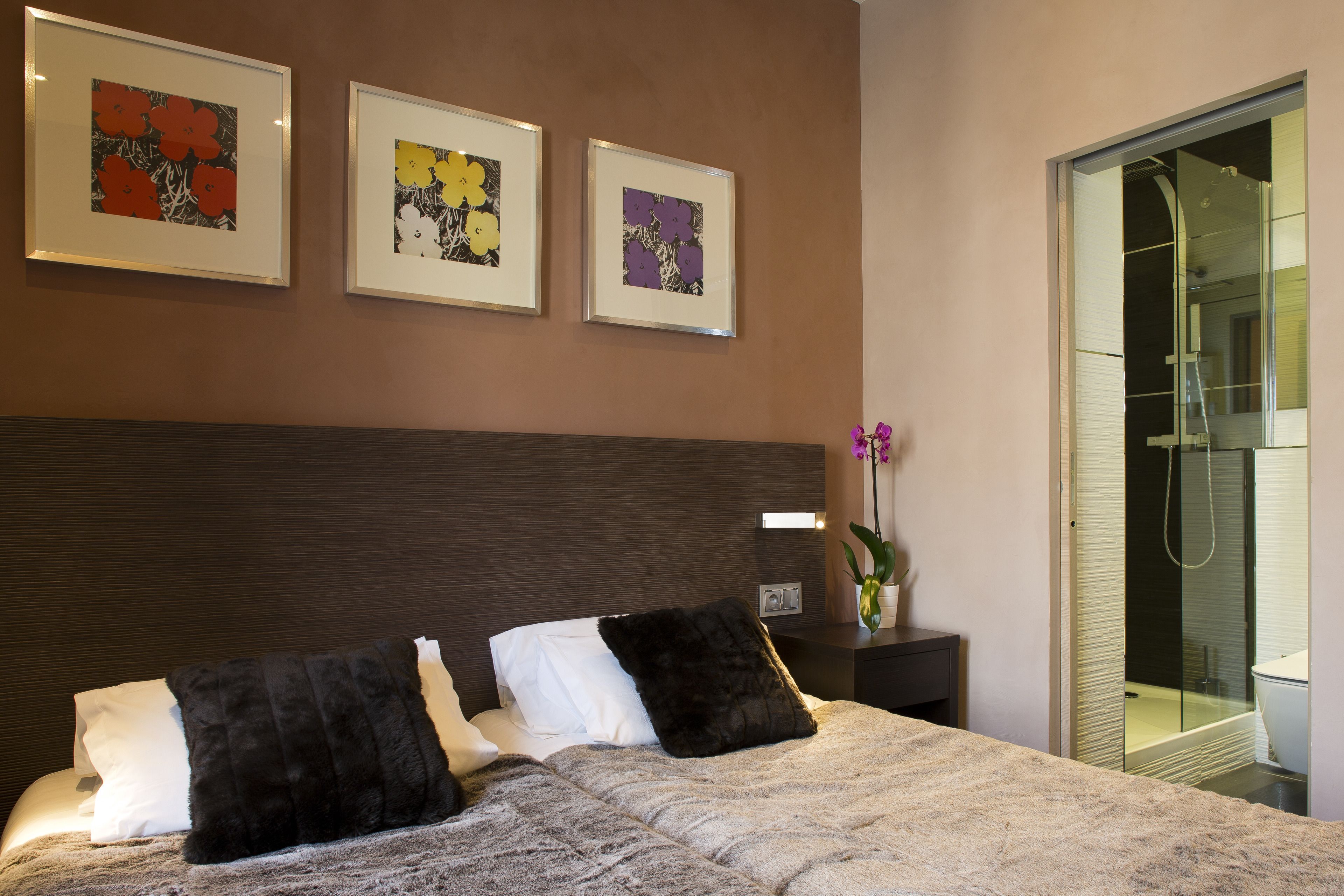 A modern bedroom with a large bed, a dark headboard, and three framed artworks on the wall.