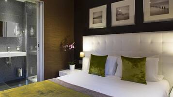 Een moderne slaapkamer met een groot bed, een douchecabine van glas en drie ingelijste foto’s aan de muur.