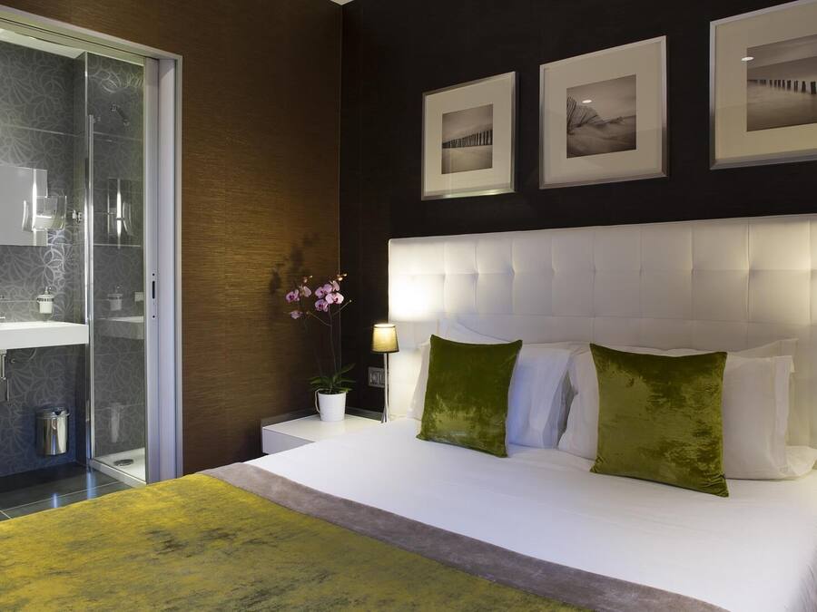 Een moderne slaapkamer met een groot bed, een douchecabine van glas en drie ingelijste foto’s aan de muur.