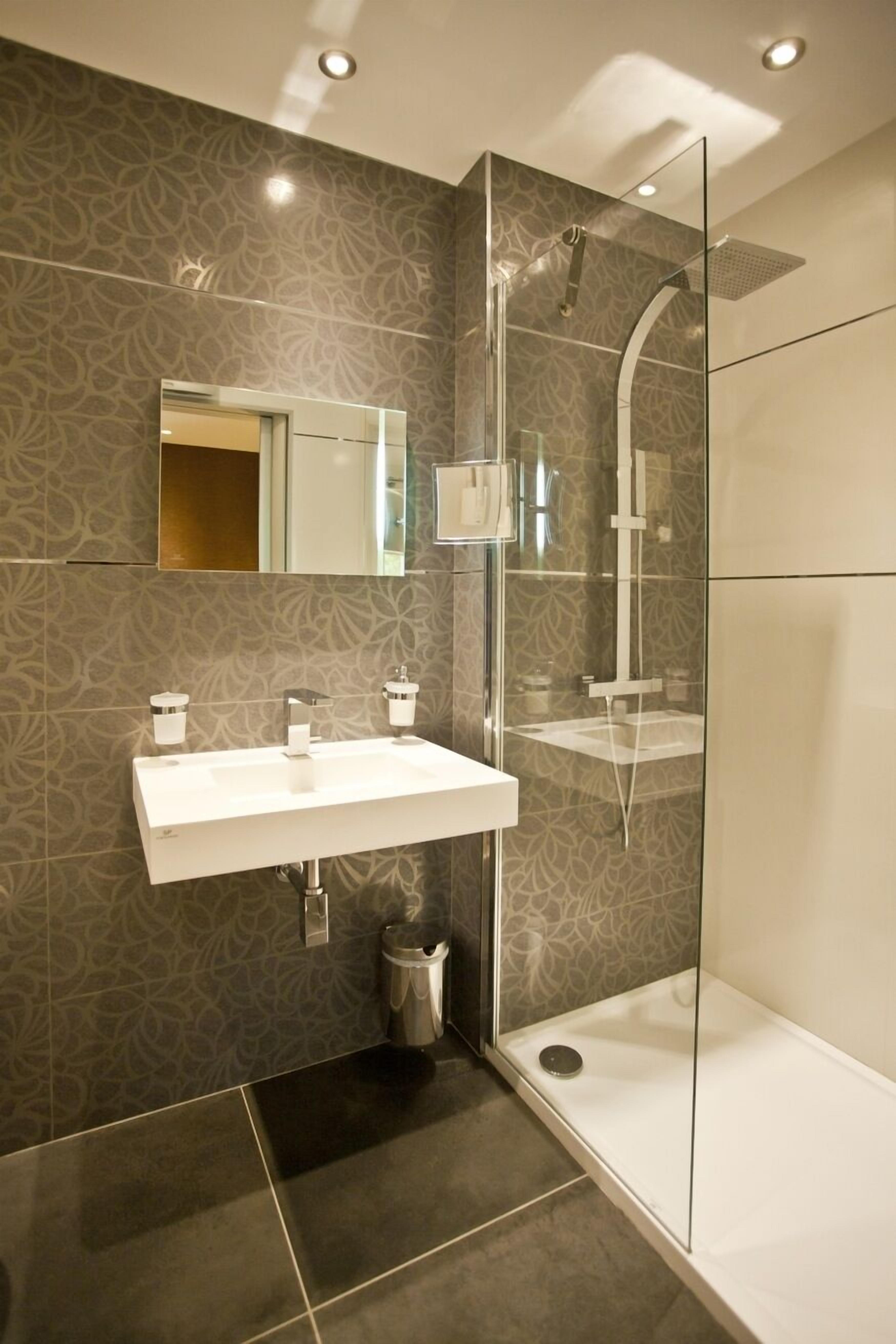 Een moderne badkamer met een douchecabine van glas, een wit wastafelmeubel en betegelde wanden.