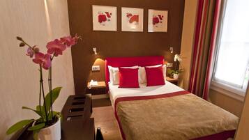 Una habitación de hotel con una cama grande, ropa de cama roja y blanca, una mesita de noche con una lámpara y una orquídea en maceta.
